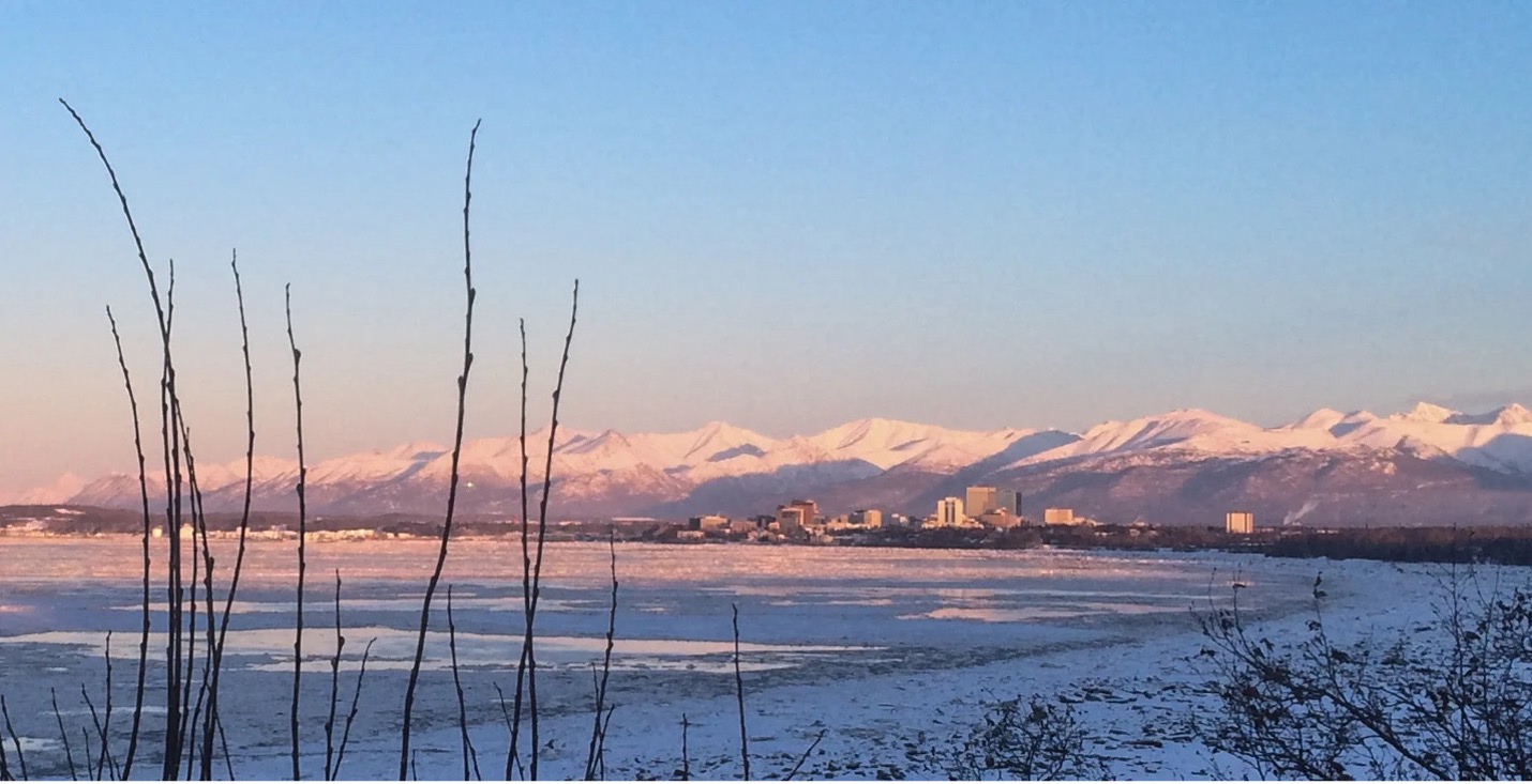 Photo of anchorage in the distance with a winter sunrise and mountains in the background