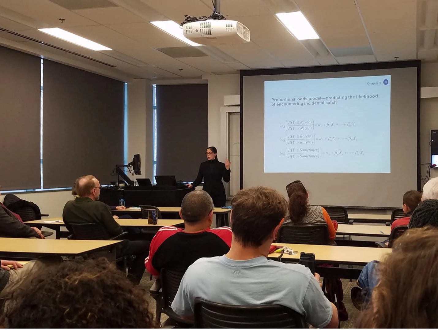 Photo of elizabeth figus at the front of a classroom with a slide presentation behind her