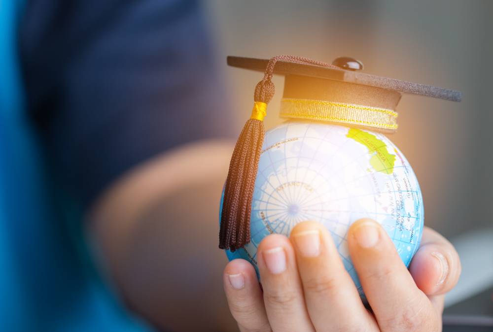 Student's hand holding small globe with a grad cap on top of it