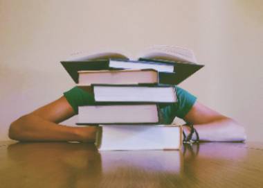 Stock image of student hiding face behind stack of books