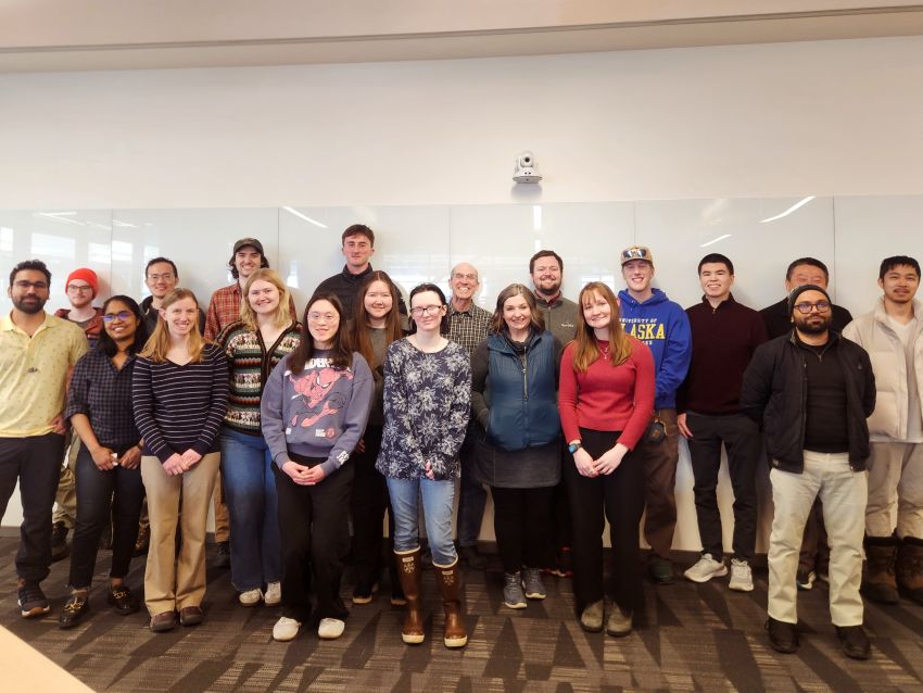 20 students and faculty pose for a group photo in front of a whiteboard