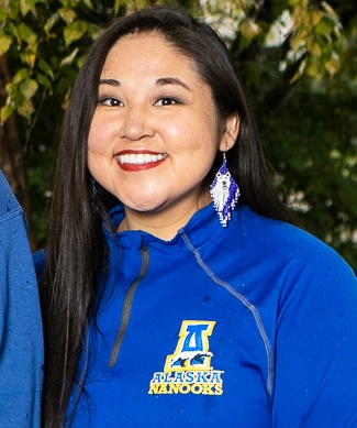 Woman with long dark hair smiles at the camera. She is wearing a blue UAF jacket and blue beaded earrings.