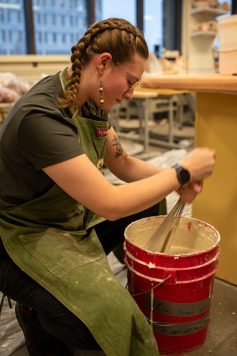 Art student Lizzy Hahn dips natural material into a bucket of porcelain slip during the hands-on workshop. Photo courtesy of Jillian Muni