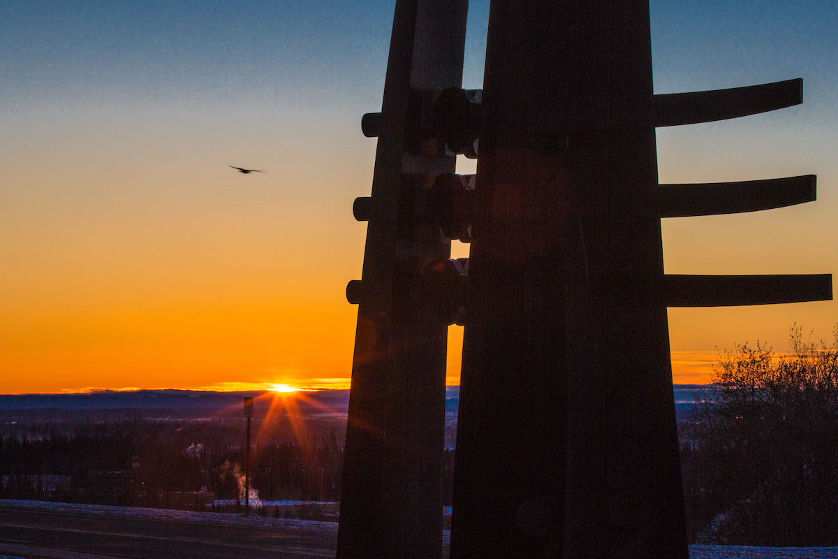 The sun rises above the Alaska Range at about 10 a.m. on Nov. 7. The photograph, taken outside the UA Museum of the North, features the sculpture "Totem," created by Bernard Hosey in 1986, in the foreground.. UAF Photo by Todd Paris