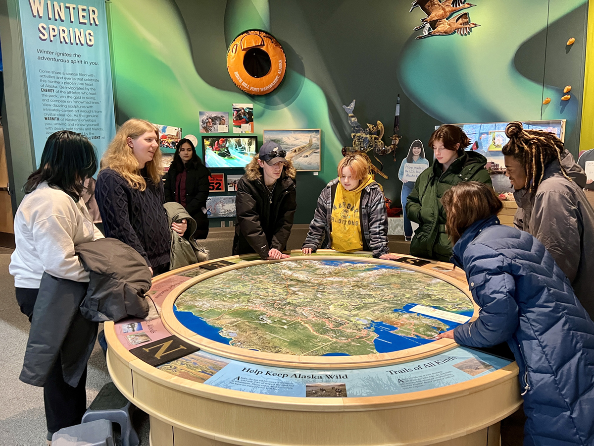Students gather around a circular map in the Morris Thompson Cultural Visitors Center. Photo by Carol Gray