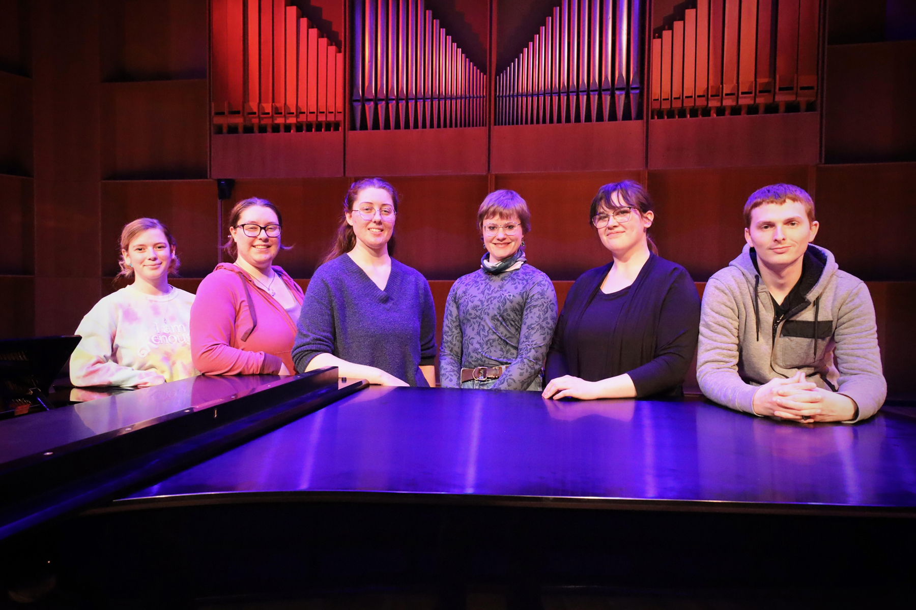 Six music students pose behind a piano in the Davis Concert Hall. Photo courtesy of Jaunelle Celaire