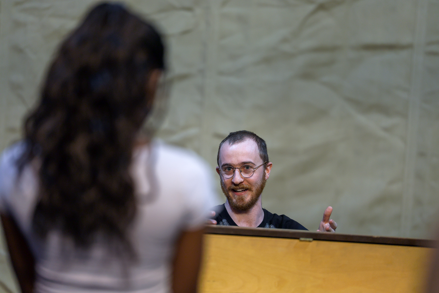 Phil Heilbron sits behind a wood upright piano, gesturing while speaking to actor Zaniyah Chestnut. Photo courtesy of the UAF Department of Theatre & Film