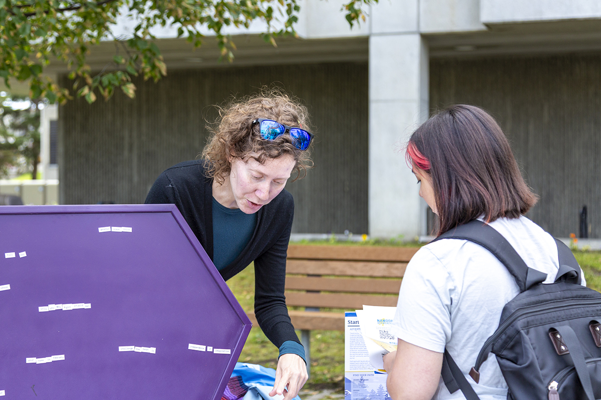 Gwen Retterer explains how the magnetic poetry activity works to a new student at UAF's 2025 Party in the Park.