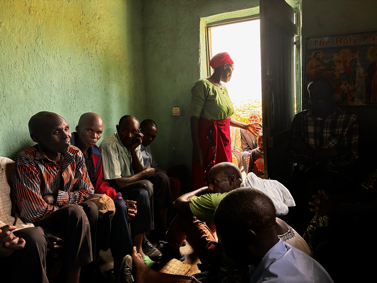 Participants gather for a dialogue session during a community-based peacebuilding workshop in Kigali. They are seated closely together in a room; one woman stands, addressing somebody through an open door.