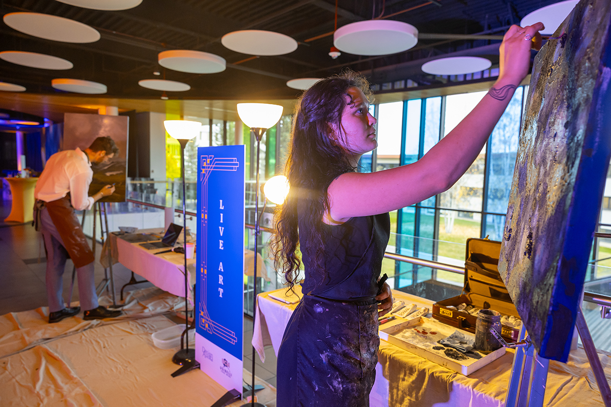 Ayona-Reily Dixon paints during a live art demonstration at the UAF Blue and Gold Gala in April 2025. Fellow art student Fin Ludwig is pictured in the background. UAF Photo by Eric Engman