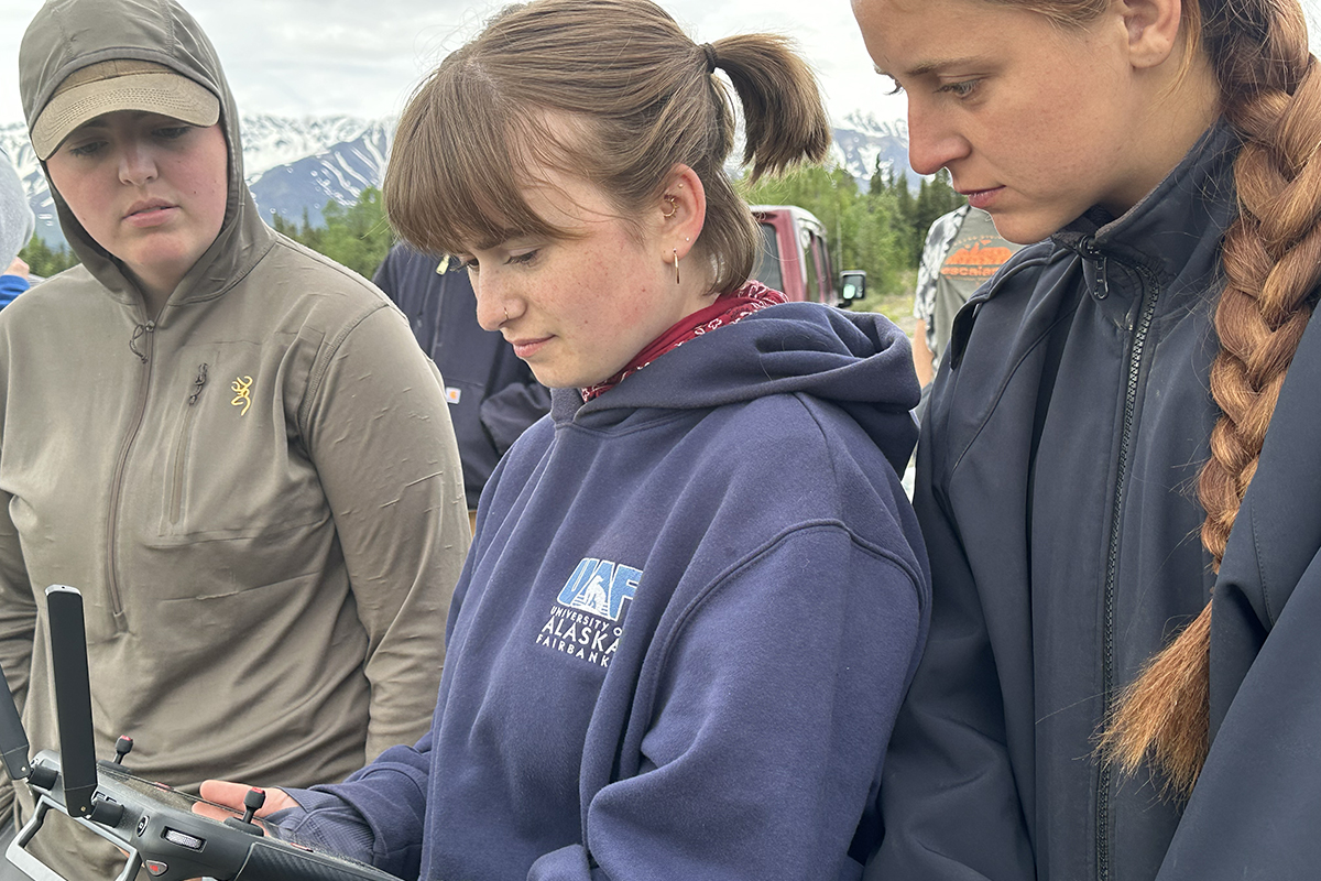 Matia Wartes (center) operates a drone to collect aerial imagery at the 2026 Anthropology Field School in Tok. Emily Owens  (left) and McKenna Kibbe (right) look on.