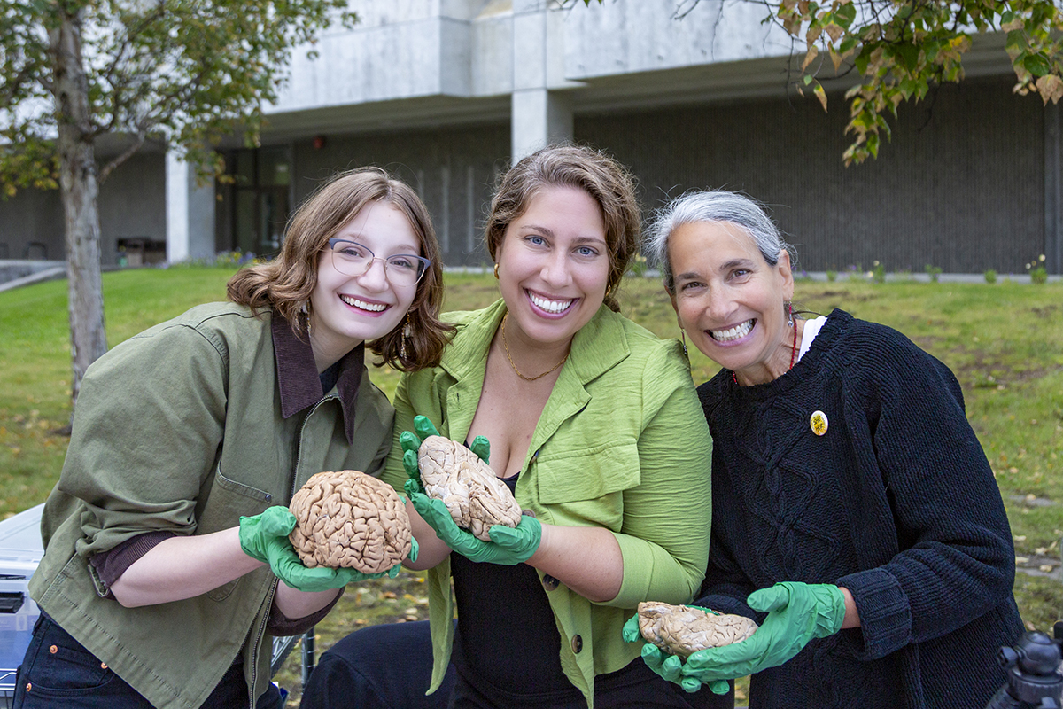 Psychology student Natalie Milburn poses with Professor Emerita Ellen Lopez, right, and Assistant Professor Christine Kindler, center, during UAF's 2025 Party in the Park. Milburn holds a brain model while Lopez and Kindler each hold one half of a brain.