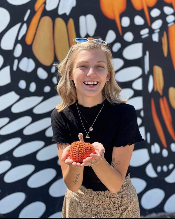 Gabby Petito holding a small knit pumpkin in front of the Monarch Mural in Ogden, Utah. 