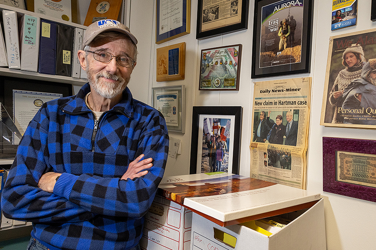 UAF Photo by Eric Engman. In his office in February 2025, Brian O’Donoghue, UAF professor emeritus of journalism, poses next to the Fairbanks Daily News-Miner from Sept. 26, 2013, featuring his front page story about the Alaska Innocence Project filing a petition to free the Fairbanks Four.