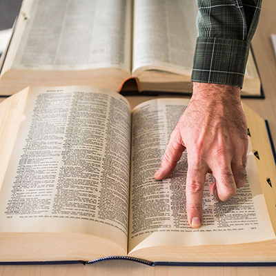 A hand hovering over an open dictionary with the index finger pointed scanning the text
