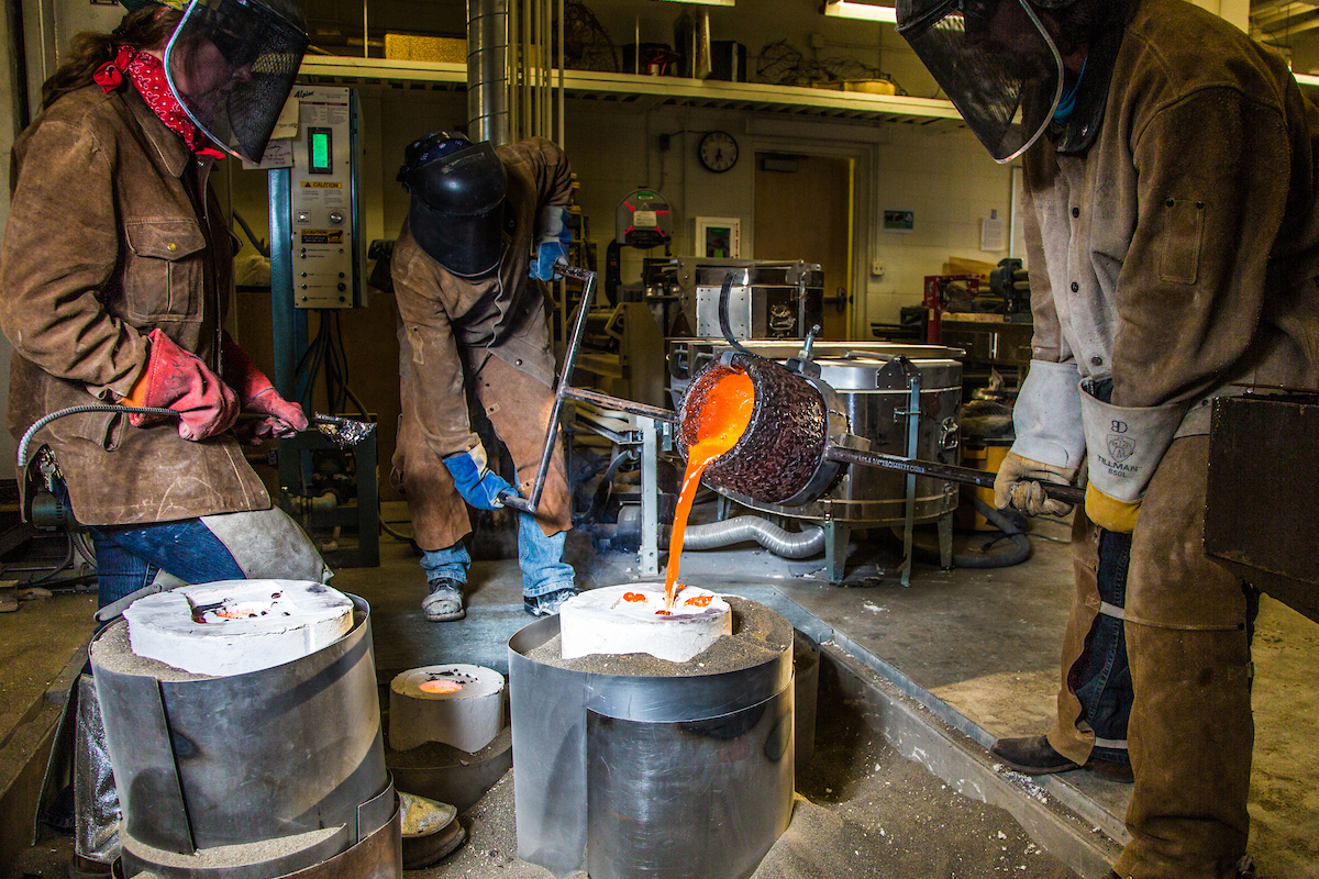 Art major Joel Isaak, center, get some help filling a mold with molten bronze as part of the process of creating a life-sized sculpture for his senior thesis in the UAF Fine Arts complex. UAF Photo by Todd Paris