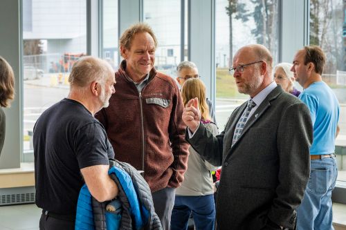 Three men in discussion in a busy building lobby with tall windows