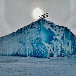 Photo of scientific instrument panels atop large ice island, sun in background. 