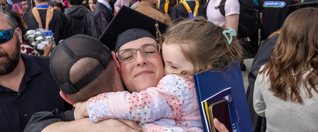 A graduating UAF student embraces their family after the 2023 commencement ceremony