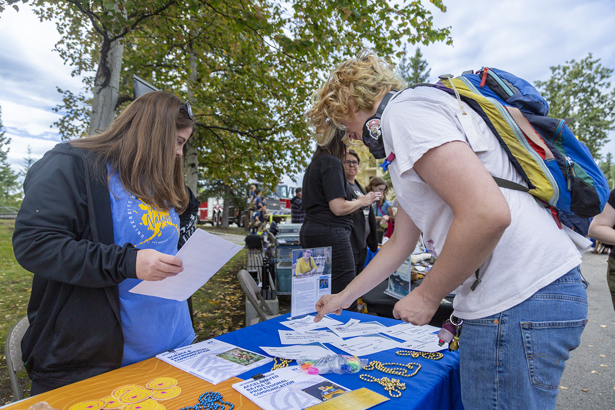 Communication department administrator Laura Foor assists an undergraduate student at the department table at the 2025 Party in the Park. UAF Photo by Sarah Manriquez