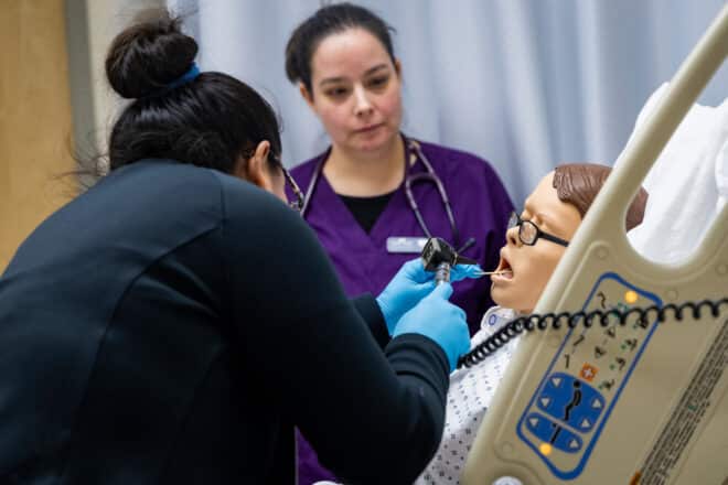 Two CTC LPN program students examine the mouth of a medical mannequin