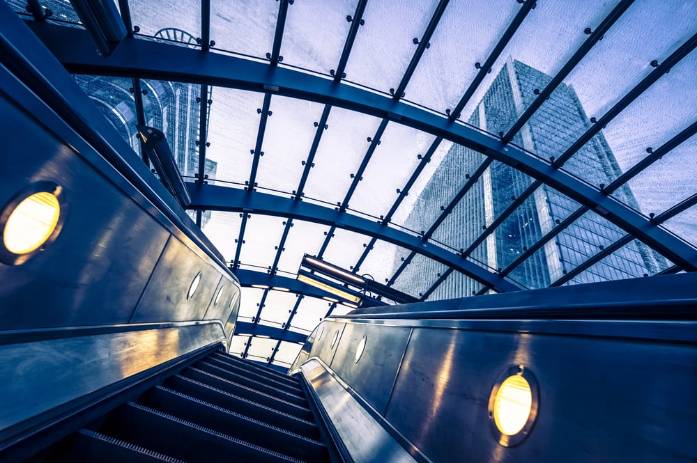 Escalator with glass ceiling looking upward on a city