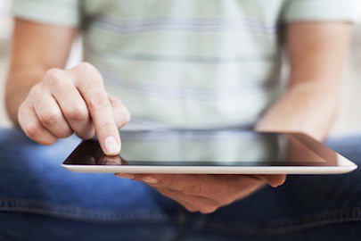 A tablet screen with a person touching the screen in the background.