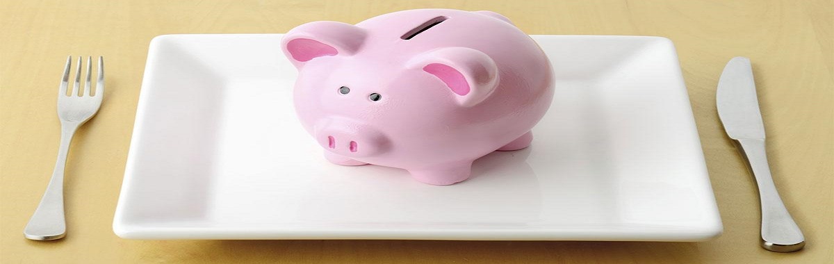 Piggy bank on a white plate with a fork and knife on either side
