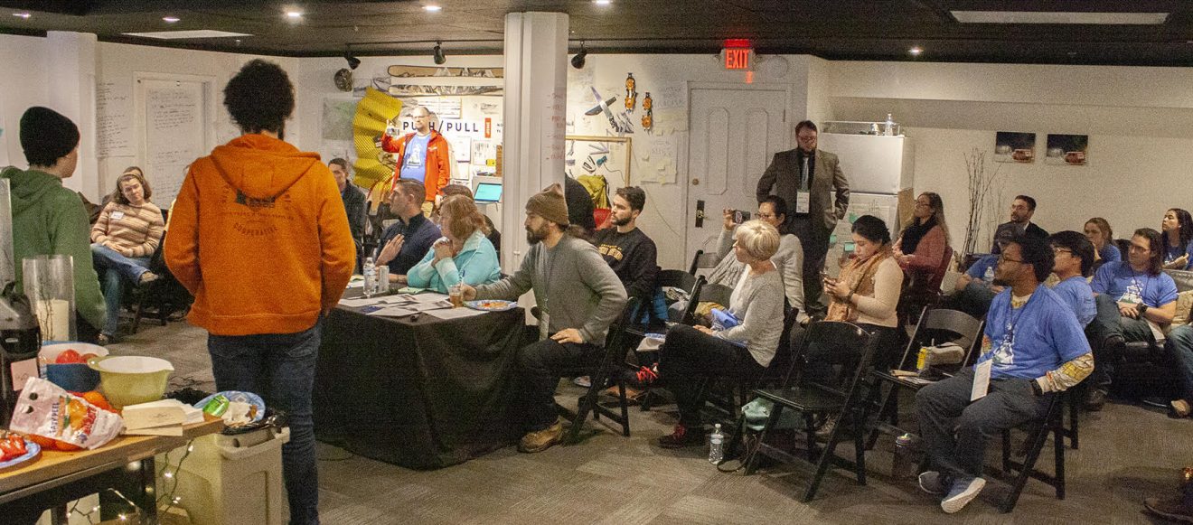 Room filled with people sitting on folding chairs listening to someone present.