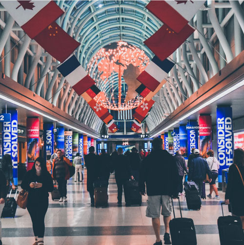People walking through an airport with flags, lights and ads around them.