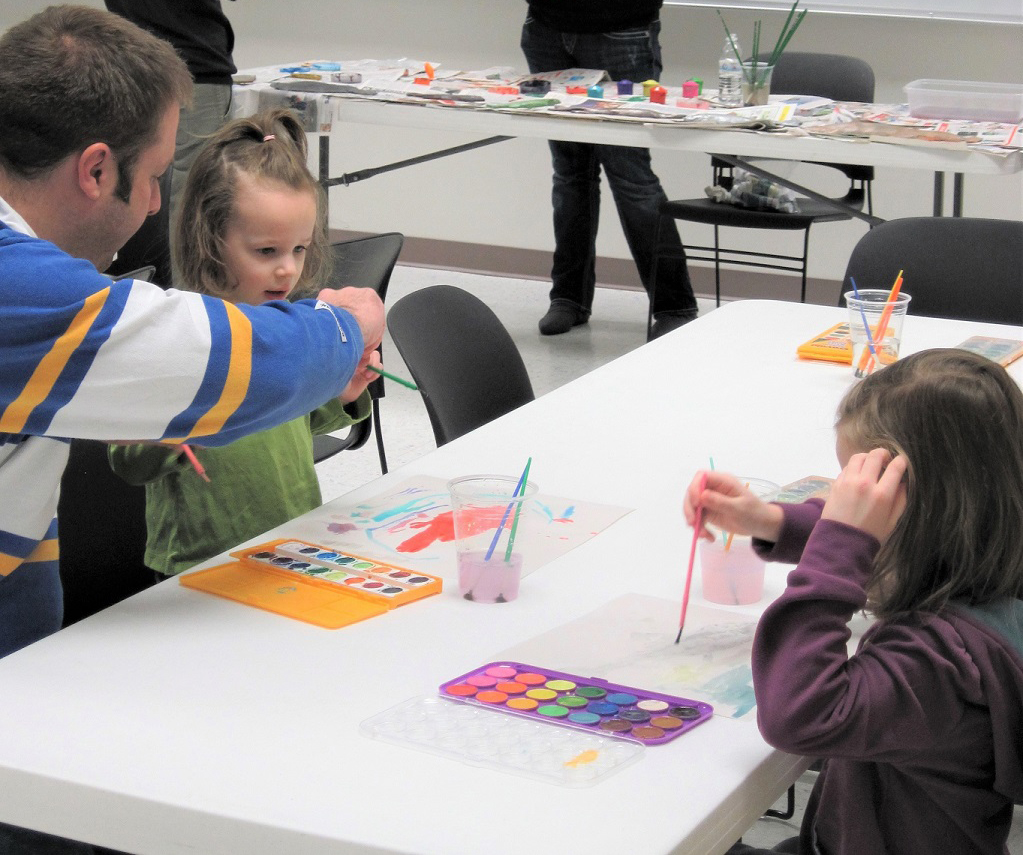 children sitting at a table painting with watercolor paints