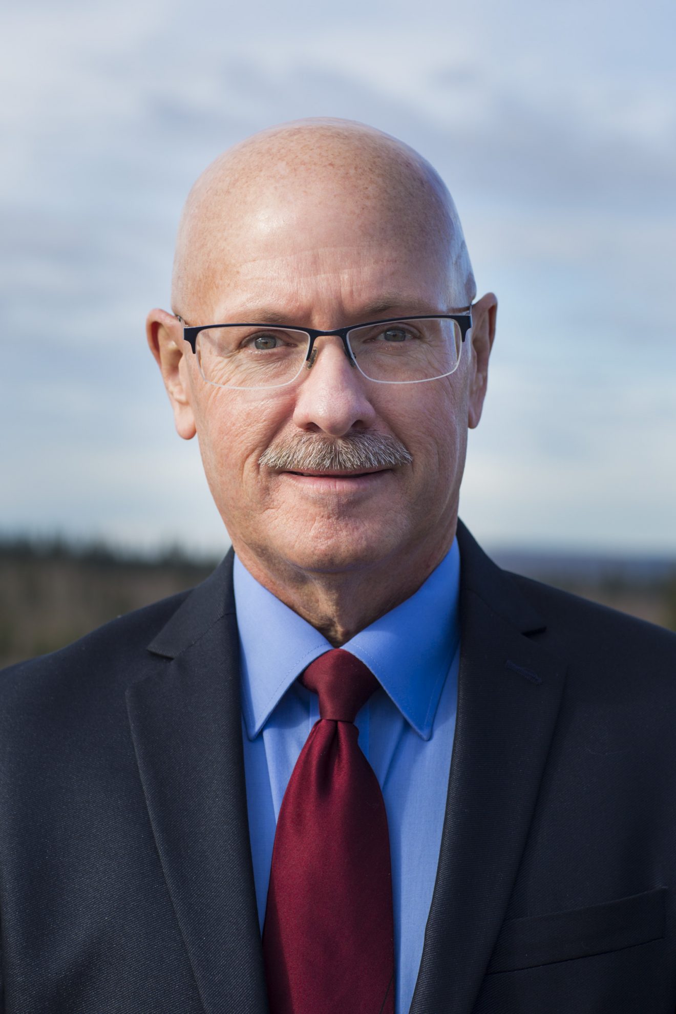 Head shot of Keith Martin. He is wearing a suit and tie, standing outside.