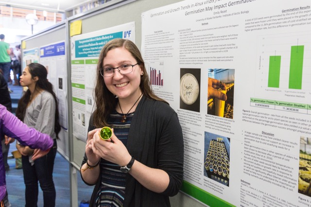 Emily Reast stands by a poster board holding what might be a small sprouting plant.