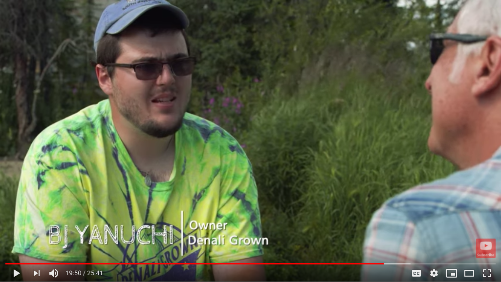 BJ Yanuchi is wearing a T-shirt, cap and sunglasses, outside. It is summer. The interviewer is wearing a blue plaid shirt and sunglasses.