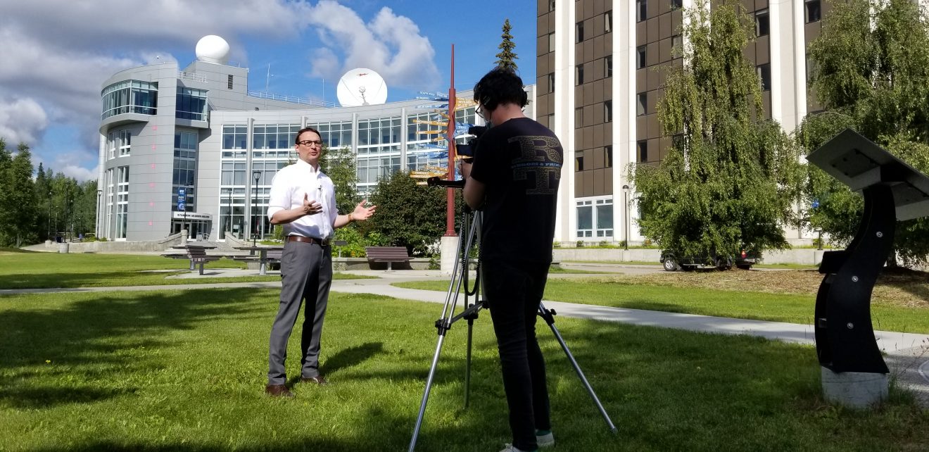 Franz Meyer talking to a camera operator in front of the Akasofu Building on a summer day.