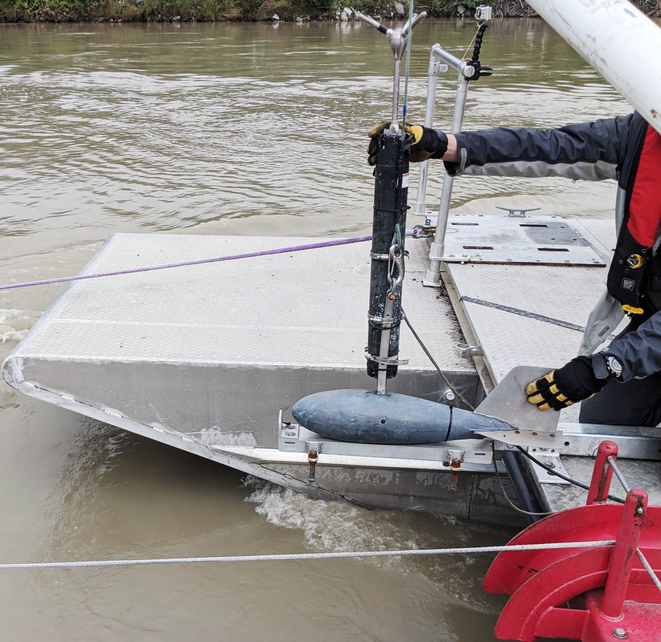 Photo of the back of a boat with a sonar device that looks like a small submarine. It is about to be placed in the river.