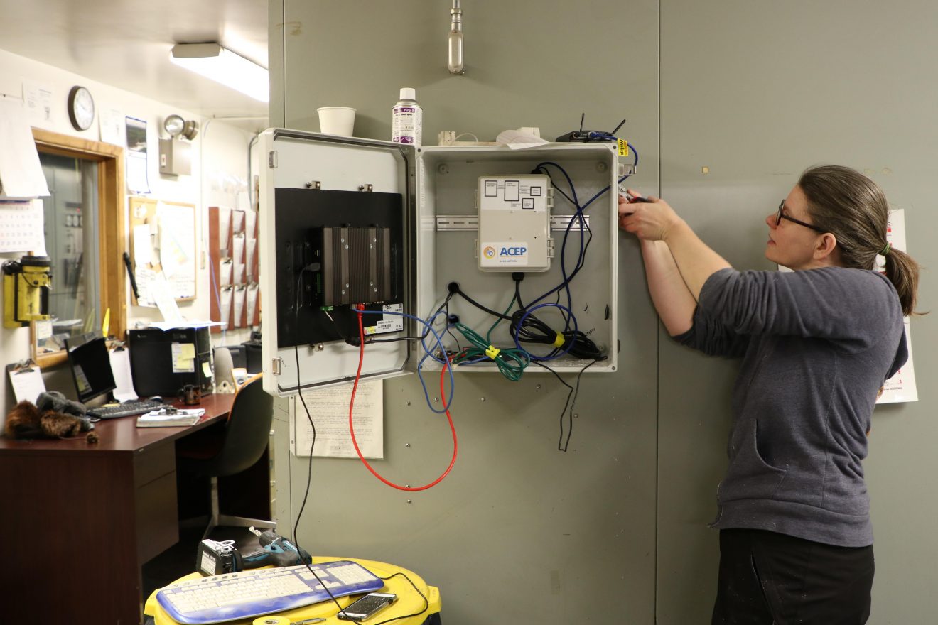 A woman works on a power box on a wall in a building.