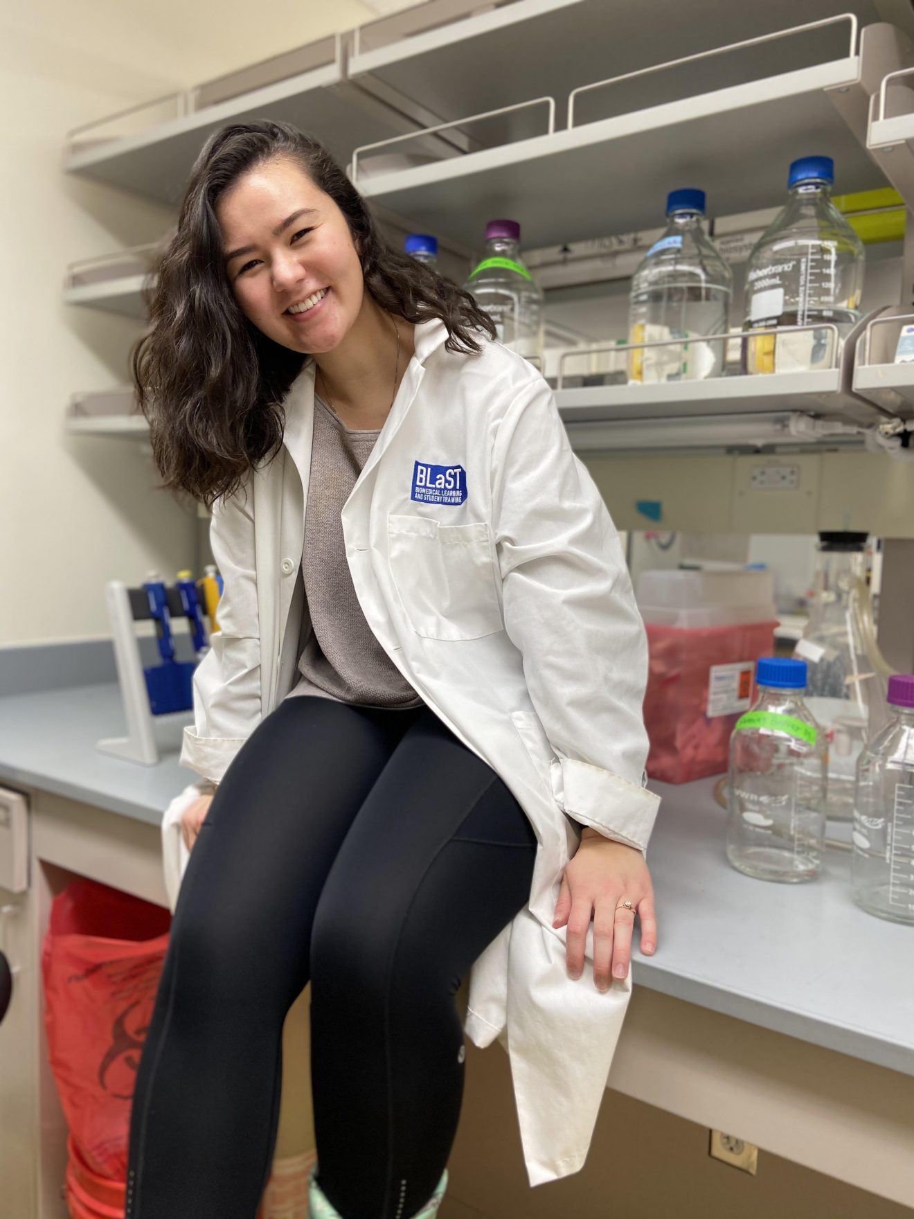 Young woman in a lab coat sitting on a workbench in a lab.