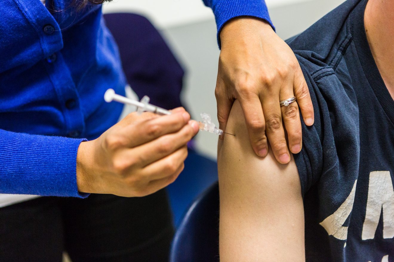 Closeup of someone administering a shot in someone's upper arm. The faces of both people are not visible.