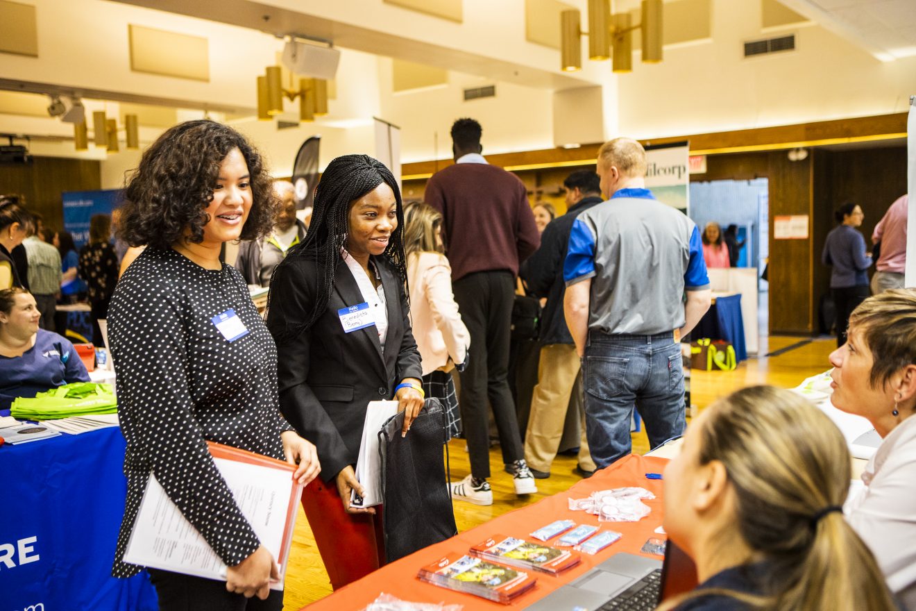 Two people speaking with people behind a table at a job fair