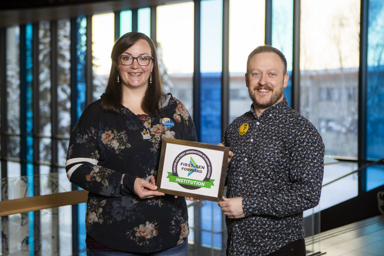 Victoria Smith and Ronnie Houchin stand together holding a small plaque in the Wood Center Dine 49 area.