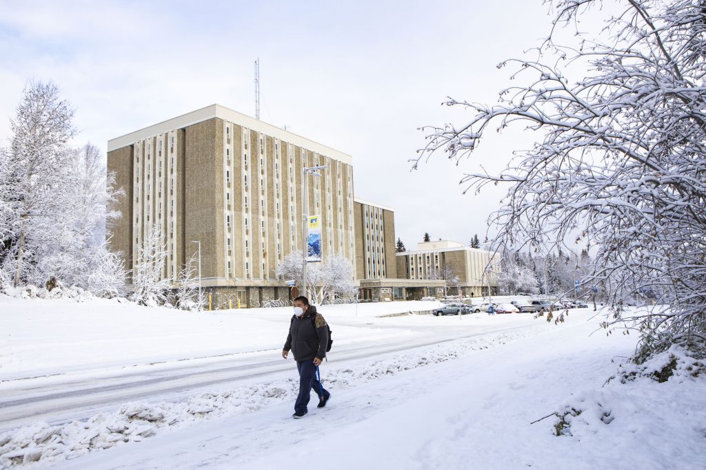 Student wearing a mask walks by a building. It is winter.
