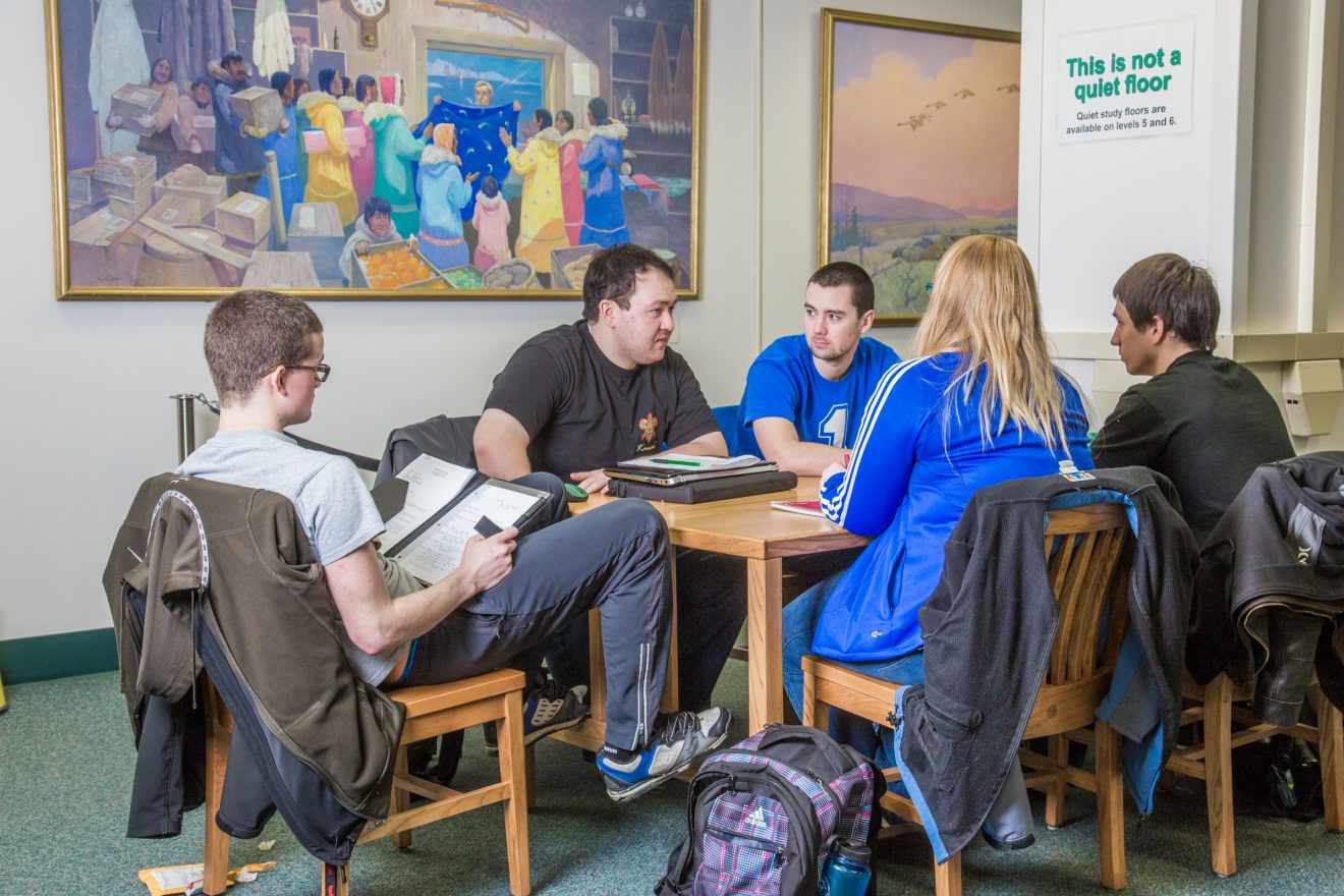 Five students sit around a table talking.