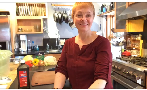 Woman standing in her kitchen. Produce sits on the counters behind her.
