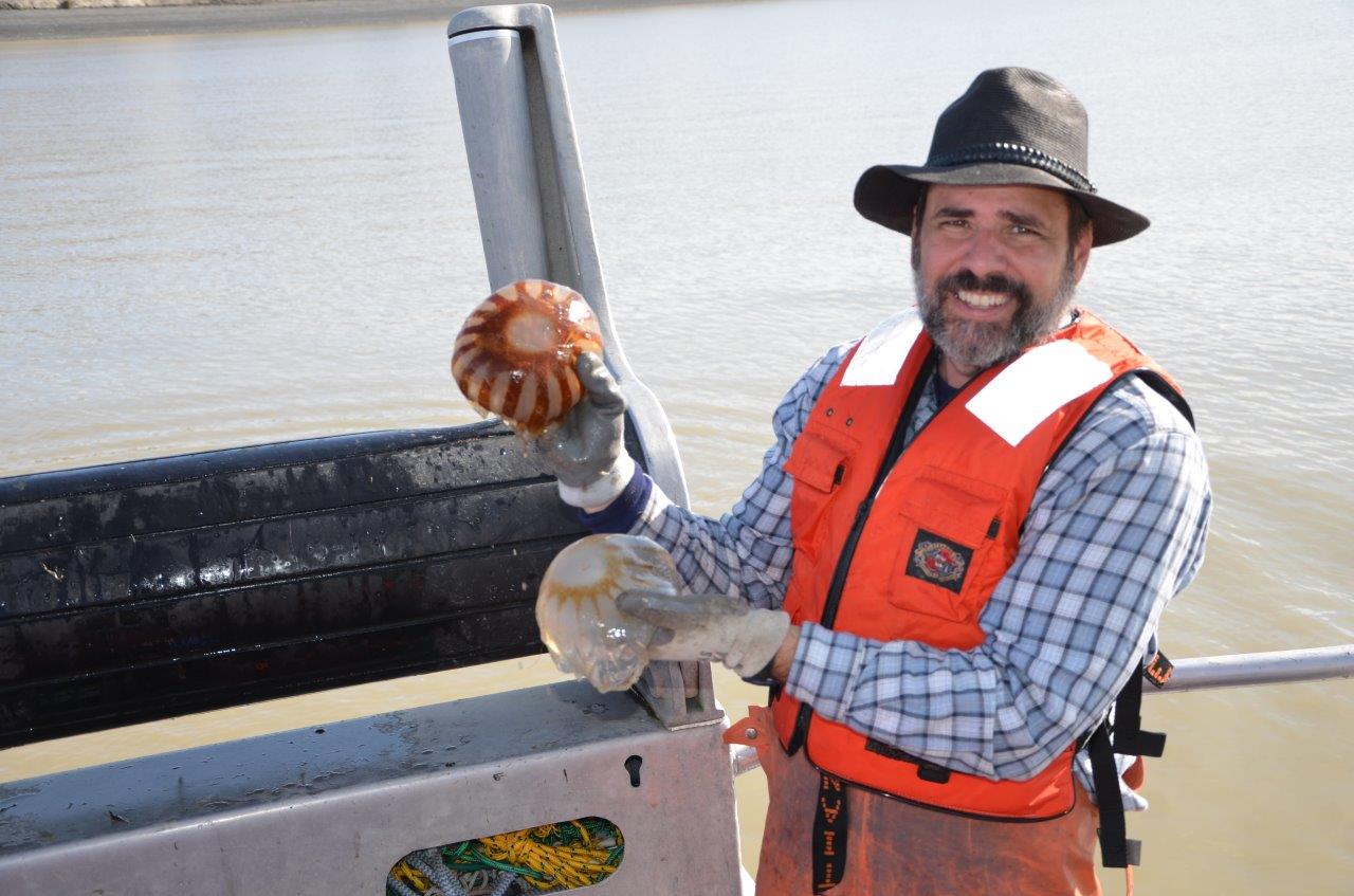 A man wearing a life jacket standing on a boat. He is holding what might be jellyfish.