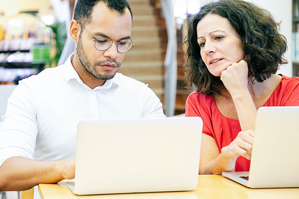 Woman leaning over to look at man's laptop screen.
