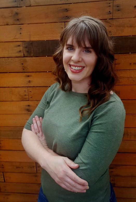 Head shot of woman standing in front of wooden wall.