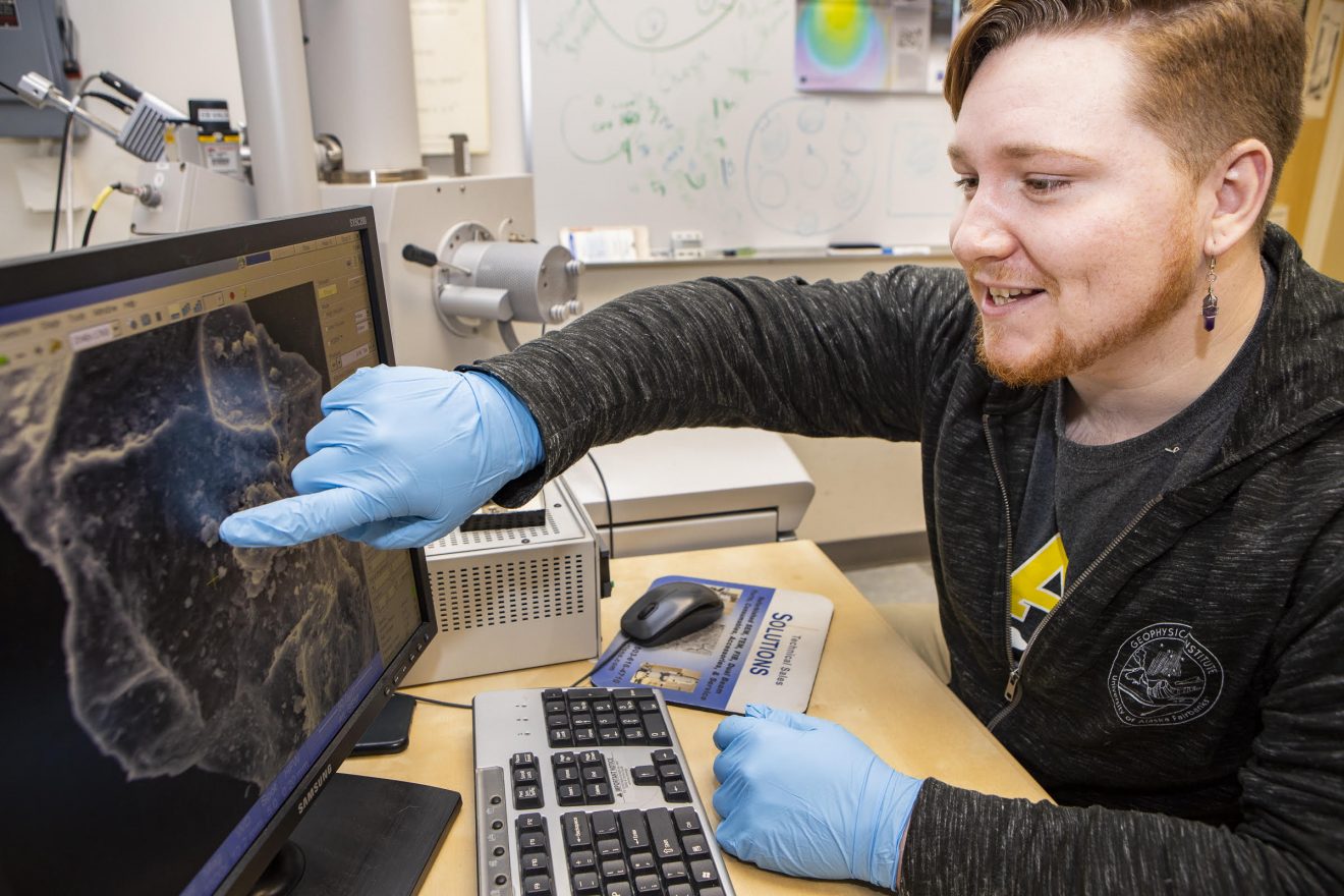 A man sits at a computer pointing at the screen.
