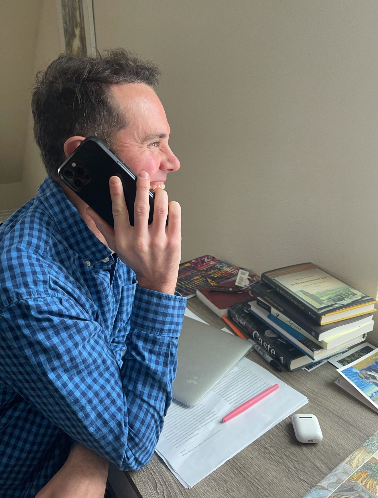 A man sitting at a desk laughing while talking on his phone.