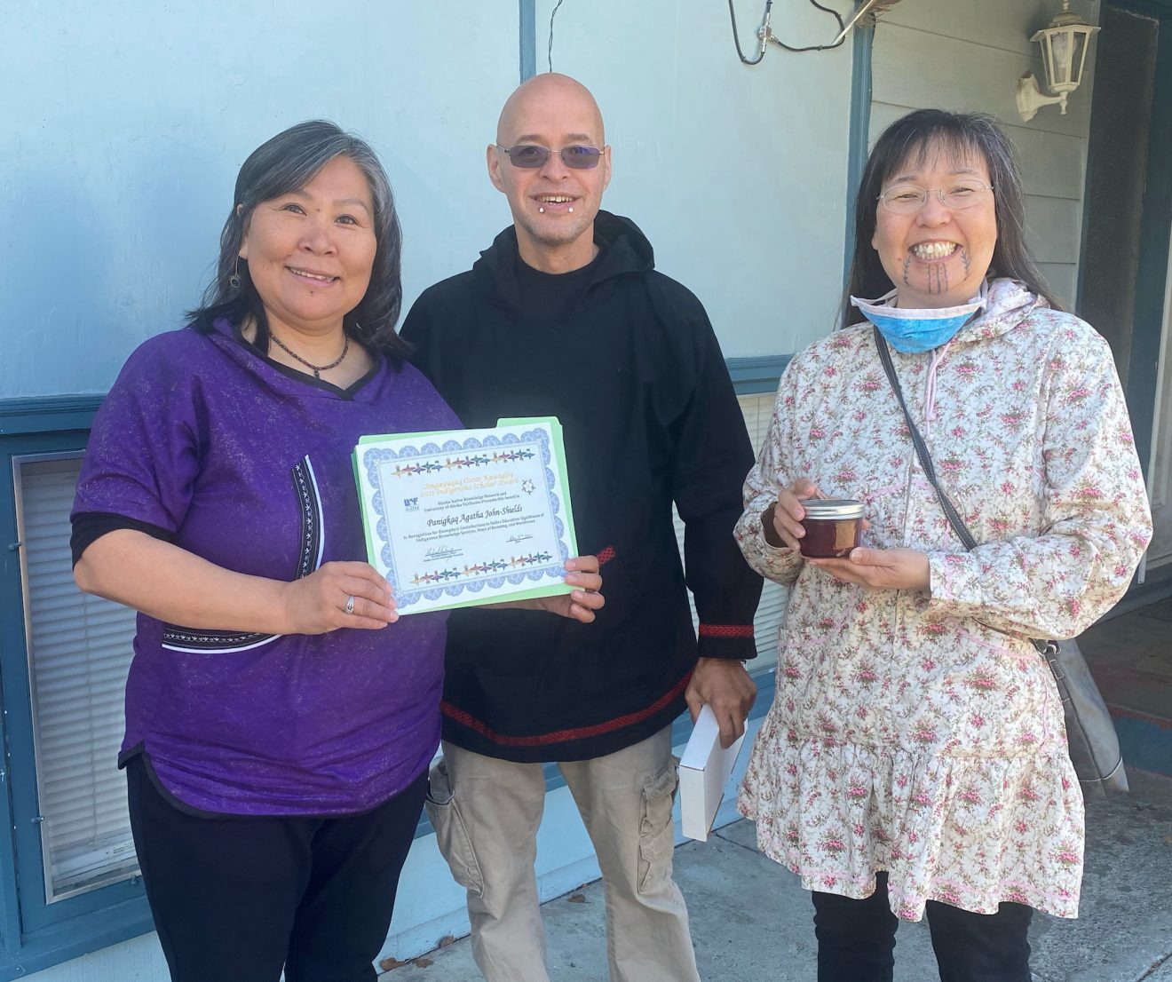 Three people stand together, one holding a certificate.